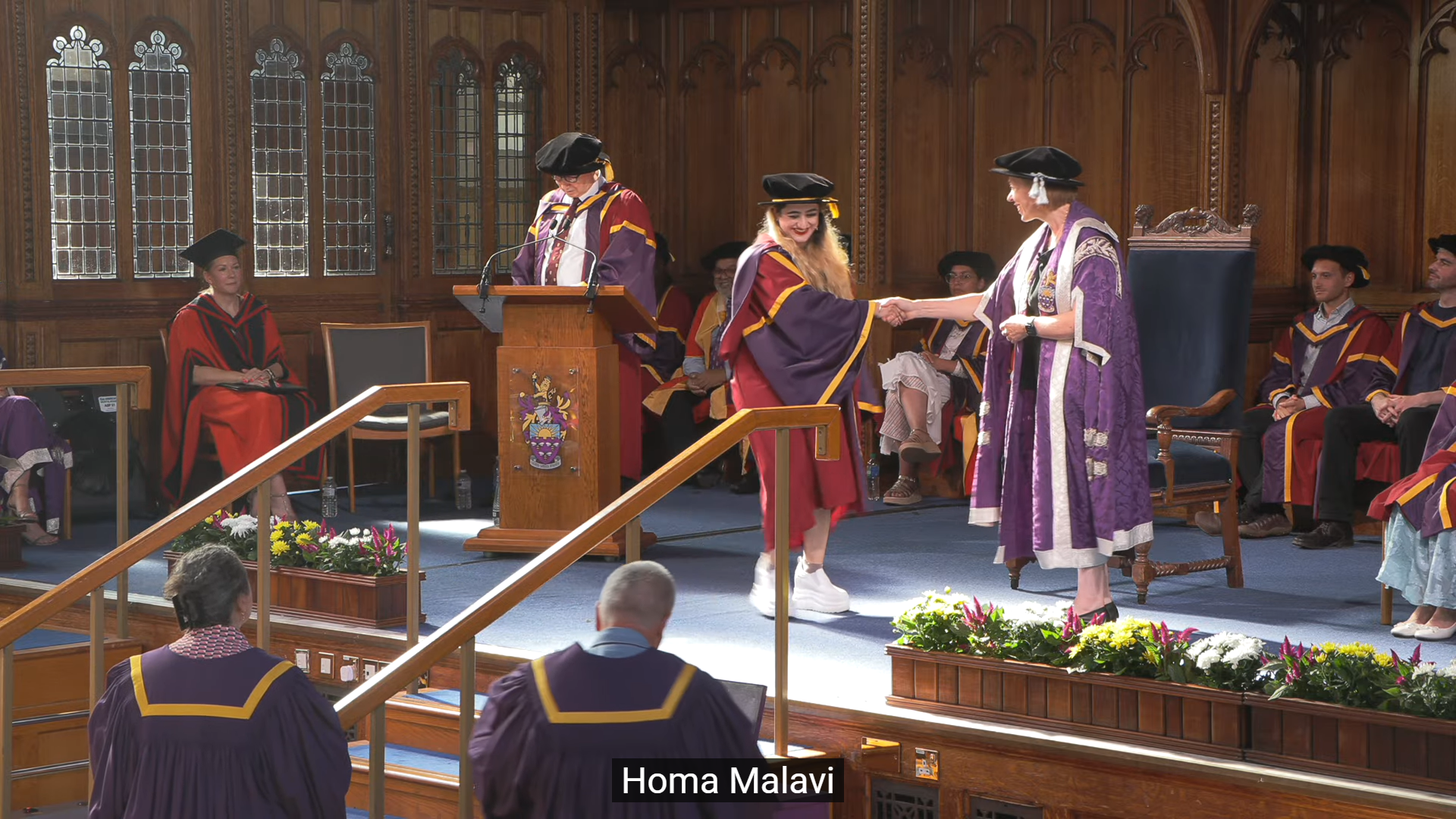 Dr. Homa Molavi being conferred her doctorate, shaking hands on stage in academic regalia